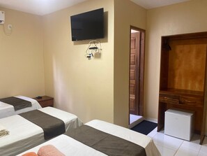 A hotel room with two beds, a television mounted on the wall, a small refrigerator, and a wooden door.