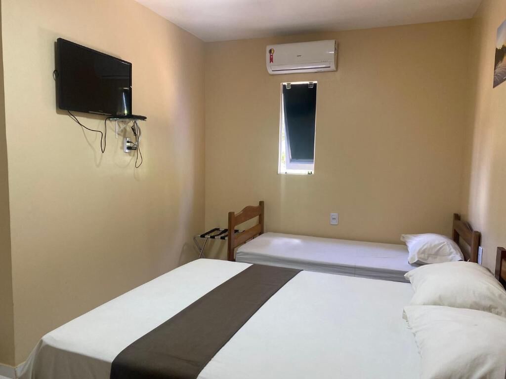 Ein Zimmer mit einem Bett, einem an der Wand befestigten Fernseher, einer Klimaanlage und einem Fenster.