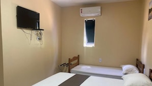 A room with a bed, a television mounted on the wall, an air conditioning unit, and a window.