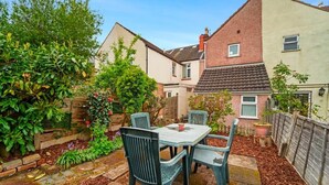 A patio with a table and chairs, surrounded by a garden and a brick wall. - Spacious 4‑Bed Home • WV1 • Family & Contractor Friendly (Wolverhampton)