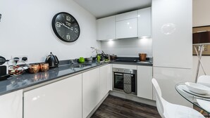 A modern kitchen with white cabinets, a black clock, and stainless steel appliances.