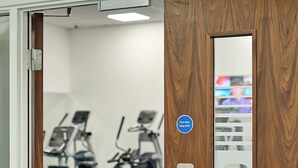 A gym with exercise equipment, a wooden door with a "Keep shut" sign, and a "Fire door keep shut" sticker.