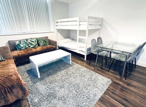 Una habitación con una cama doble, un sofá, una mesa baja y una mesa de vidrio con sillas.
