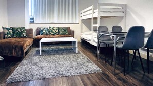 A compact room with a bunk bed, a sofa with a coffee table, and a desk with two chairs.