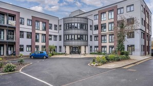 A modern multi-story building with a central atrium, parking lot, and landscaped areas. - Central Solihull 1-Bed | Parking • WiFi • NEC (Solihull)