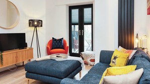 A modern living room with a flat-screen TV, a red armchair, a blue sofa, and a floor lamp. - Central Solihull 1-Bed | Parking • WiFi • NEC (Solihull)