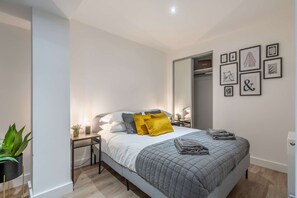 A modern bedroom with a bed, bedside tables, a mirror, and framed artwork on the wall.