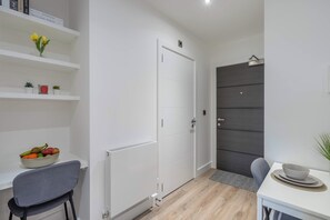 A modern, minimalistic room with white walls, a wooden floor, a white door, and a small table with a bowl and a plant.