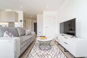 A modern living room with a grey sofa, a round coffee table, and a flat-screen TV on a white cabinet.