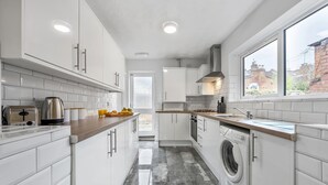 A modern kitchen with white cabinetry, a built-in washing machine, and a window with a view of the outside.