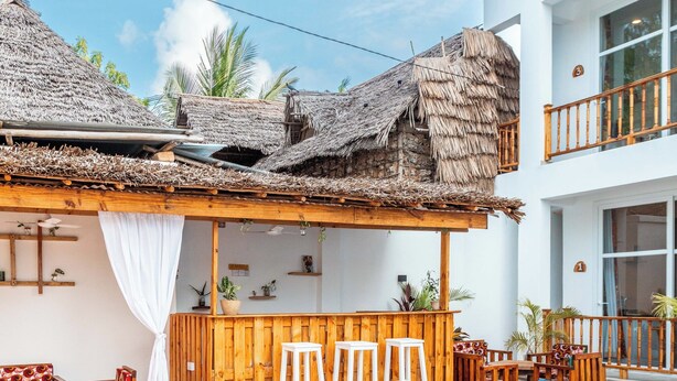 A pool area with wooden furniture, a bar, and a thatched-roof structure. - Mimea Boutique villa  (Jambiani)