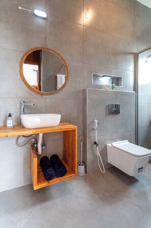 A modern bathroom with a wooden vanity, a round mirror, a white sink, and a glass shower enclosure. - Mimea Boutique villa  (Jambiani)