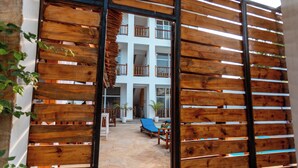 A wooden gate leading to a courtyard with a lounge area, potted plants, and a multi-story building in the background. - Mimea Boutique villa  (Jambiani)