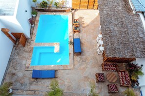 A rooftop swimming pool with stone flooring, blue lounge chairs, and a thatched roof area. - Mimea Boutique villa  (Jambiani)