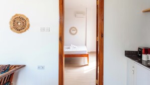 A room with a bed, a wooden door, a kitchen area with a microwave, and a wall-mounted air conditioner. - Mimea Boutique villa  (Jambiani)