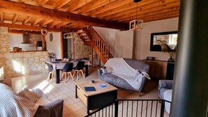A cozy living room with a stone wall, wooden ceiling beams, a dining area with a table and chairs, and a staircase leading to an upper level. - La Grange, gîte between land and sea. (Verlincthun)