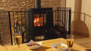 A wooden table with a stone fireplace, two glasses of wine, a bowl of nuts, and a plate with a sausage. - La Grange, gîte between land and sea. (Verlincthun)