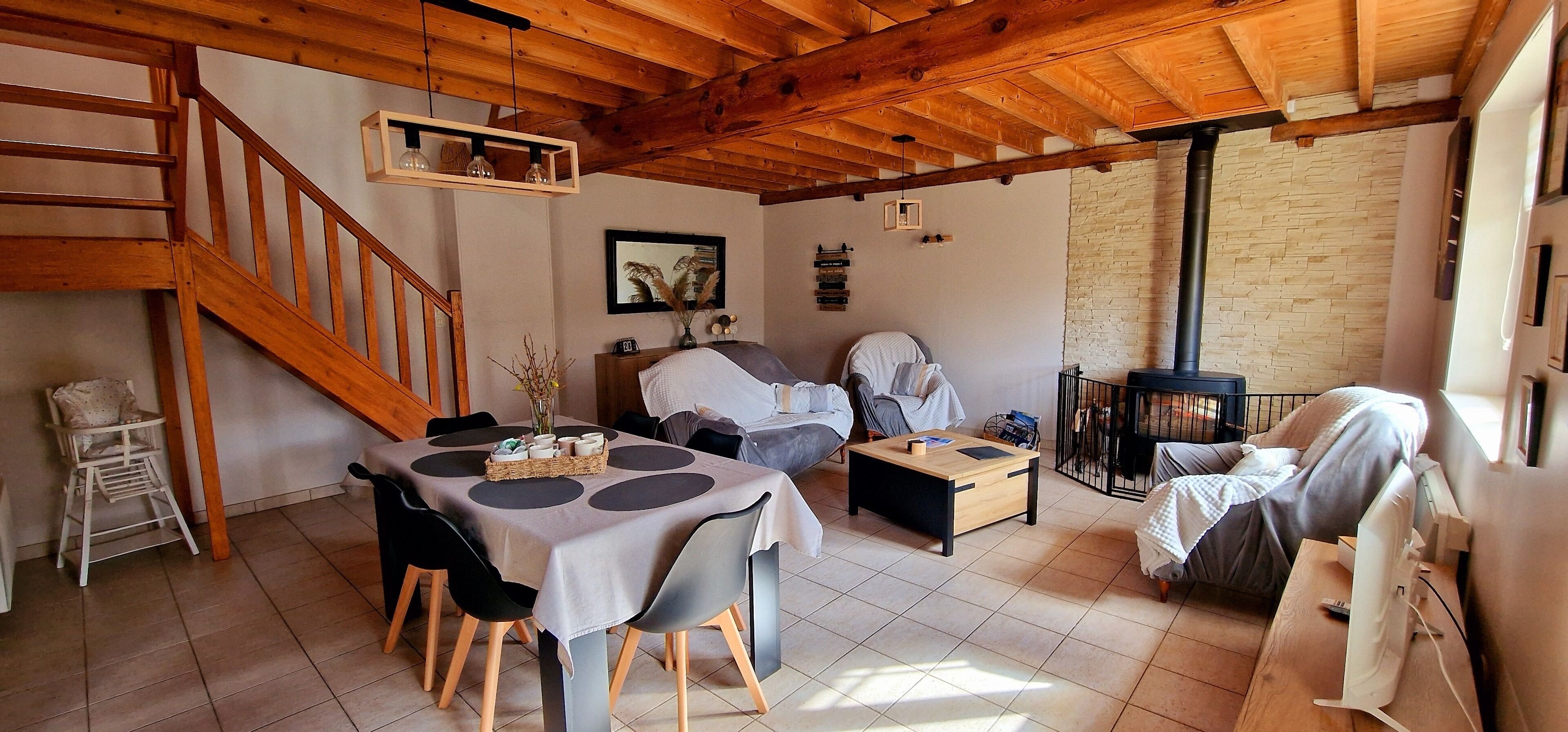 A cozy living room with a wooden staircase, a dining area with a table and chairs, a sofa, and a fireplace.