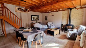 A cozy living room with a wooden staircase, a dining area with a table and chairs, a sofa, and a fireplace.