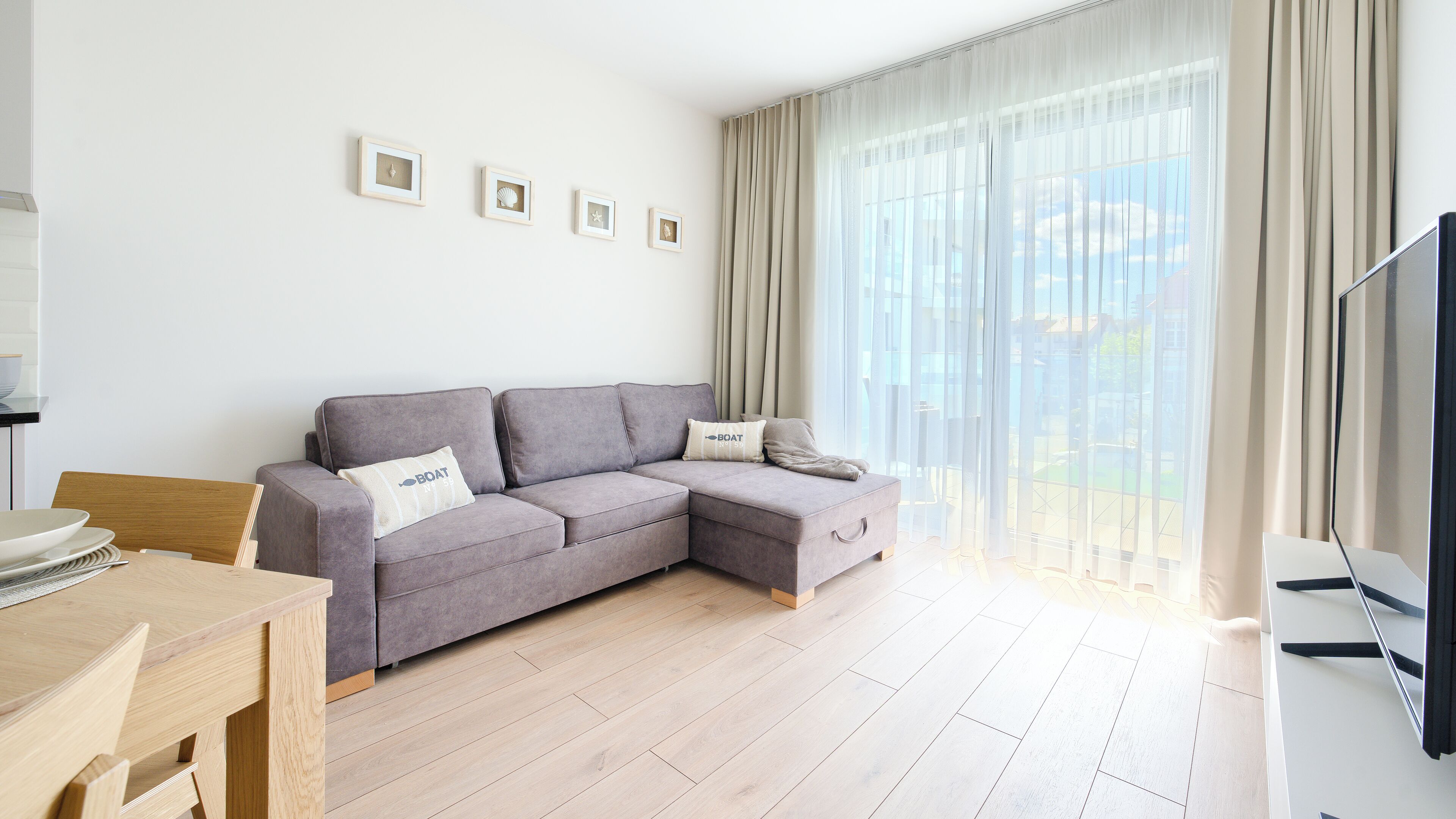 Un soggiorno moderno con un divano modulare grigio, un tavolo da pranzo in legno e una grande finestra con tende leggere.