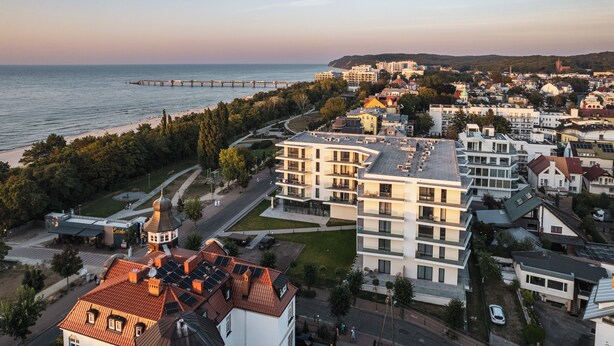 Une ville côtière dotée de bâtiments modernes, d’une jetée qui s’avance dans la mer et d’une église surmontée d’un dôme.