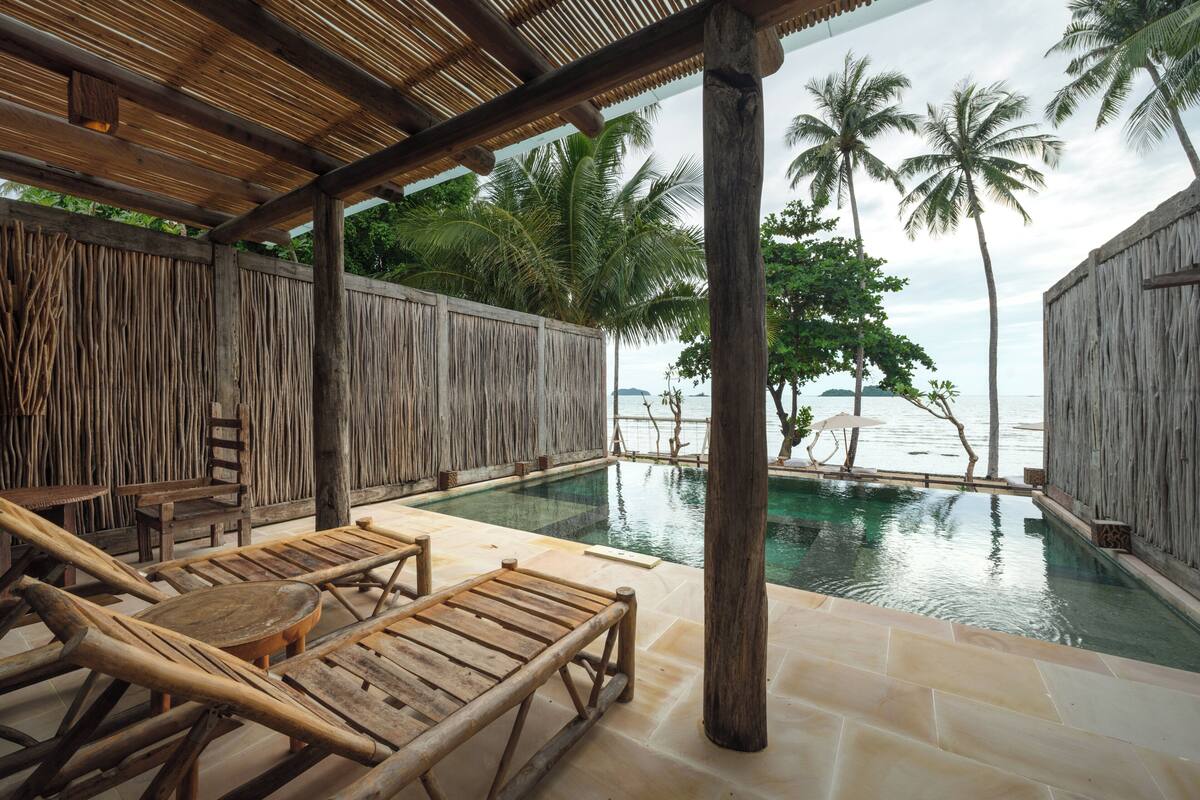 A wooden deck with lounge chairs and a pool, surrounded by palm trees and a view of the ocean.