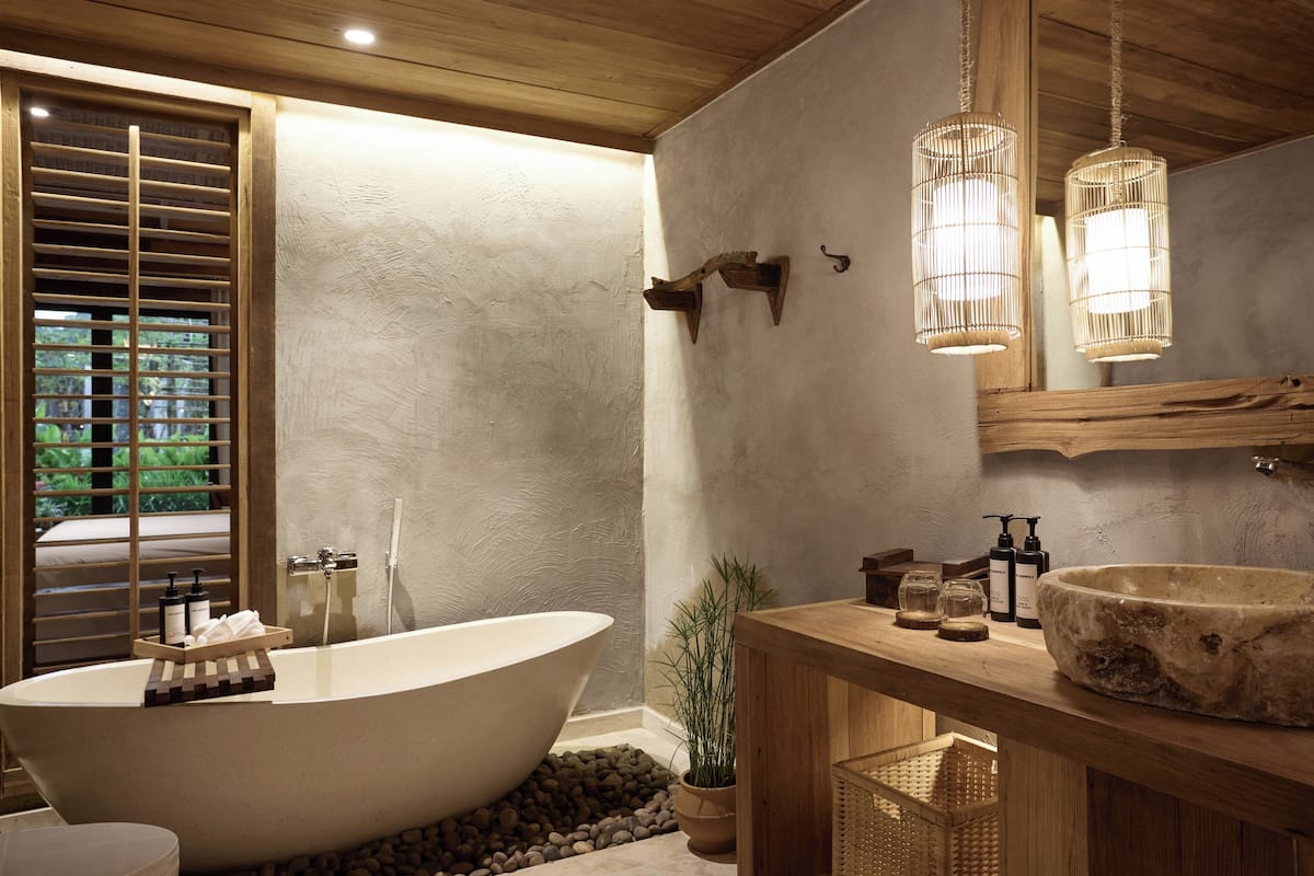 Un baño moderno con una bañera independiente, estantes de madera, un espejo grande y una lámpara colgante.
