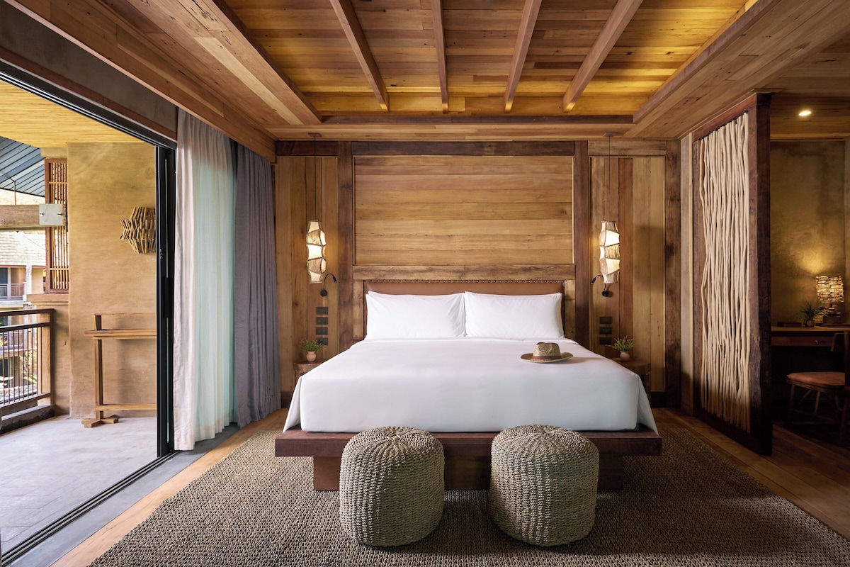 Ein Schlafzimmer mit Holzboden, einem großen Bett, zwei Nachttischlampen und Blick durch eine Glastür.