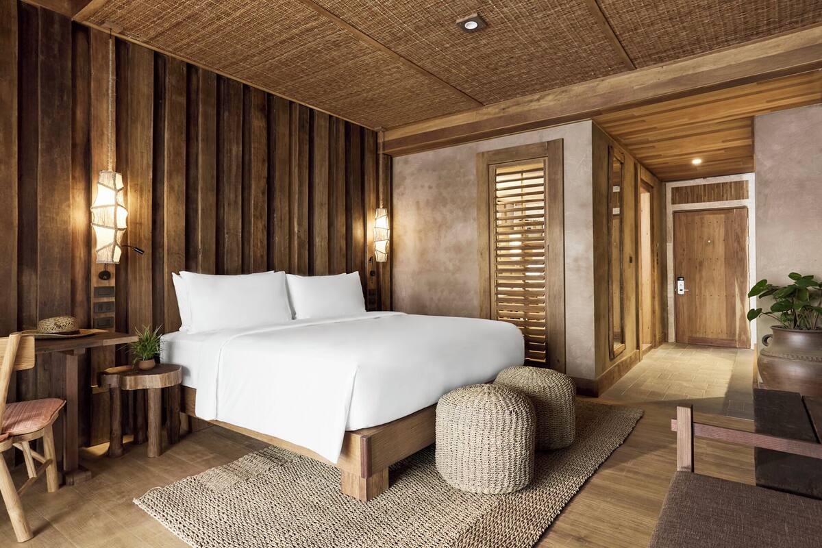 A bedroom with a wooden bed, bedside lamps, a small table, and a potted plant.