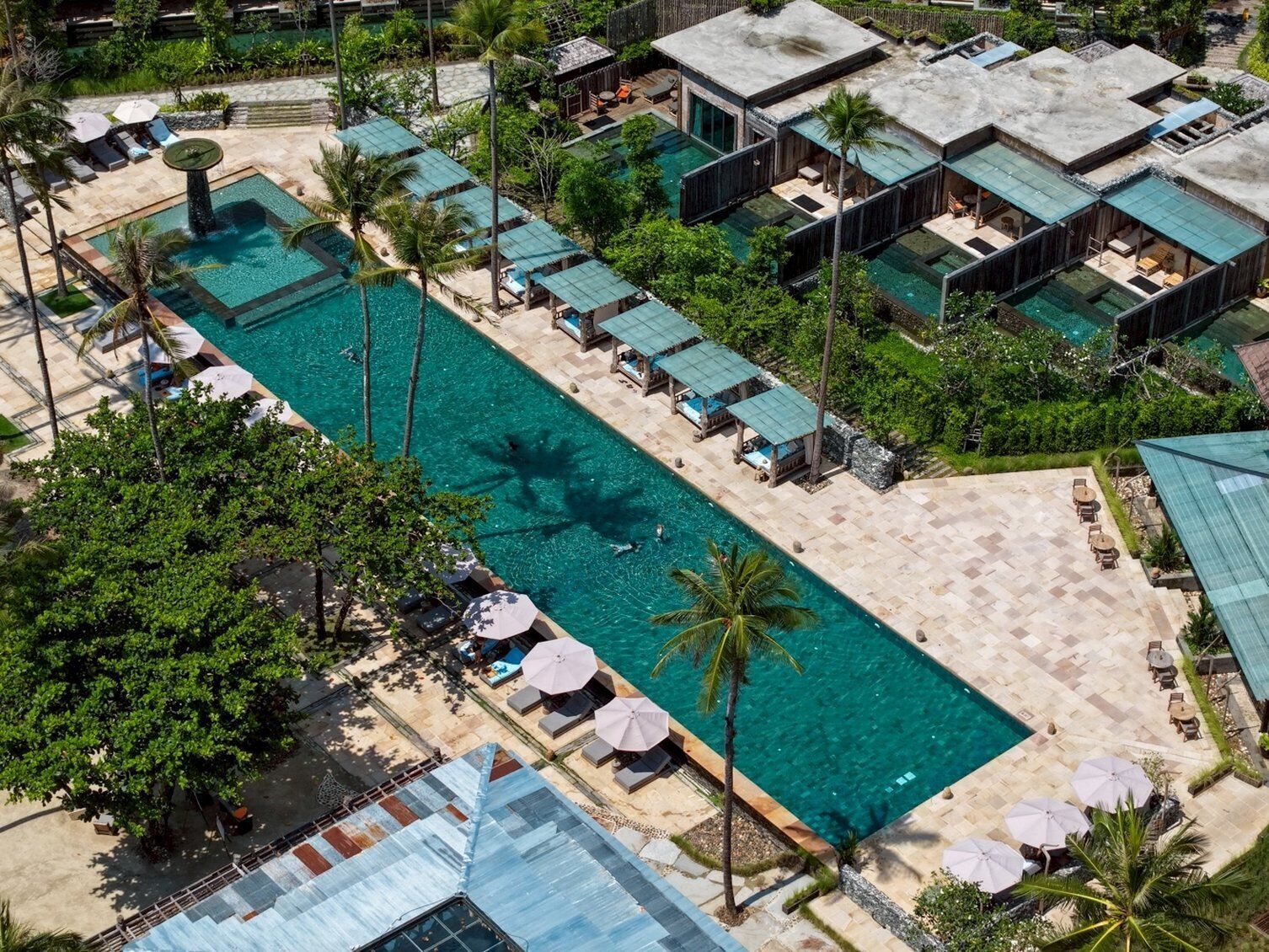 Vista aérea de un complejo turístico con una gran piscina, varias habitaciones de huéspedes con piscinas privadas y exuberante vegetación.