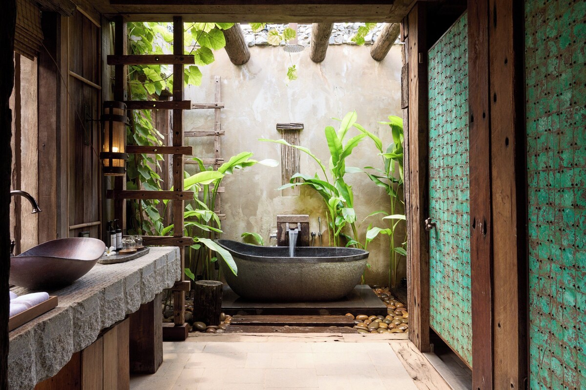 A rustic bathroom with a large stone sink, a bathtub, and a wooden shelf.