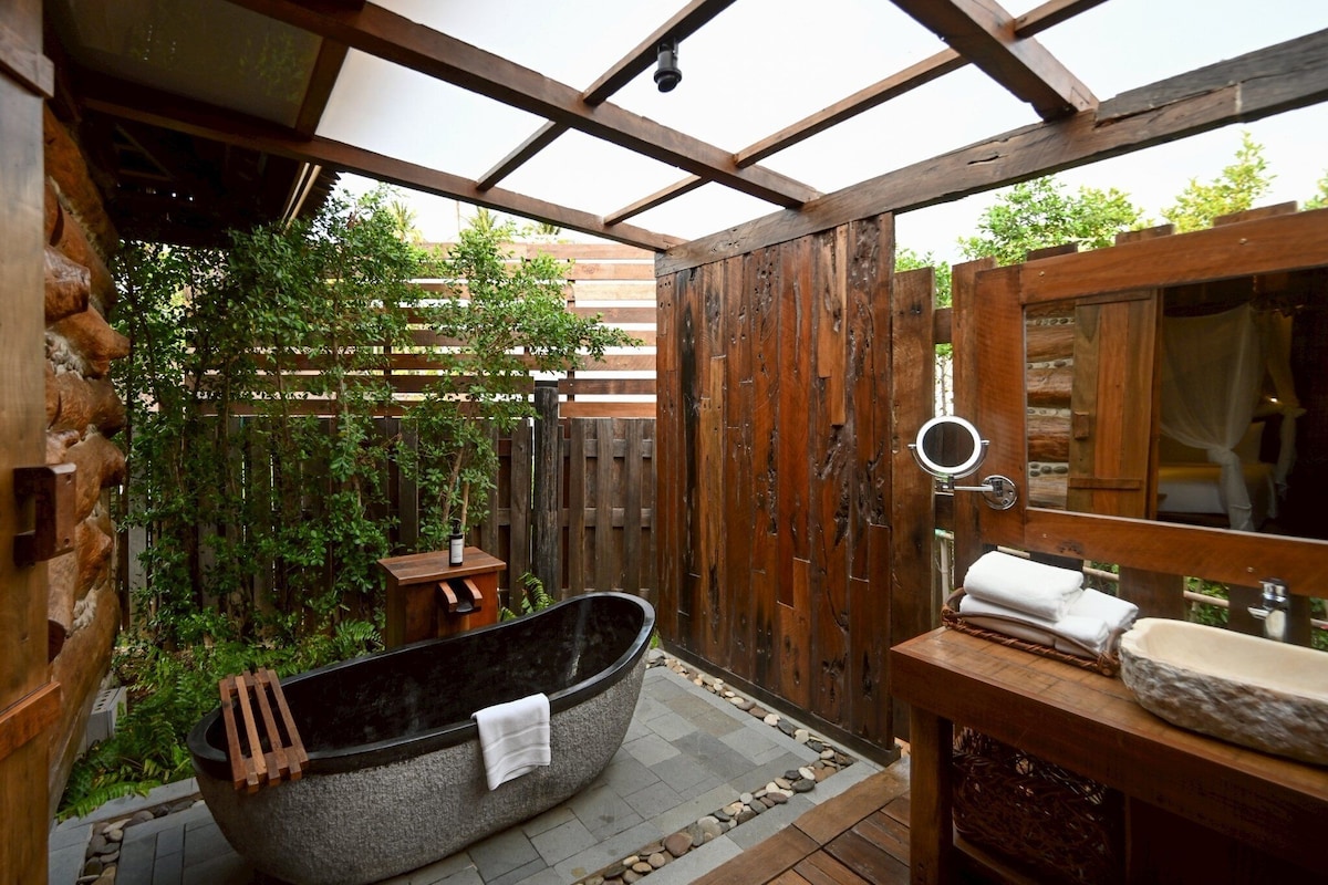 Ein rustikales Badezimmer mit freistehender Badewanne, einem Holzausleger und einem großen Spiegel.