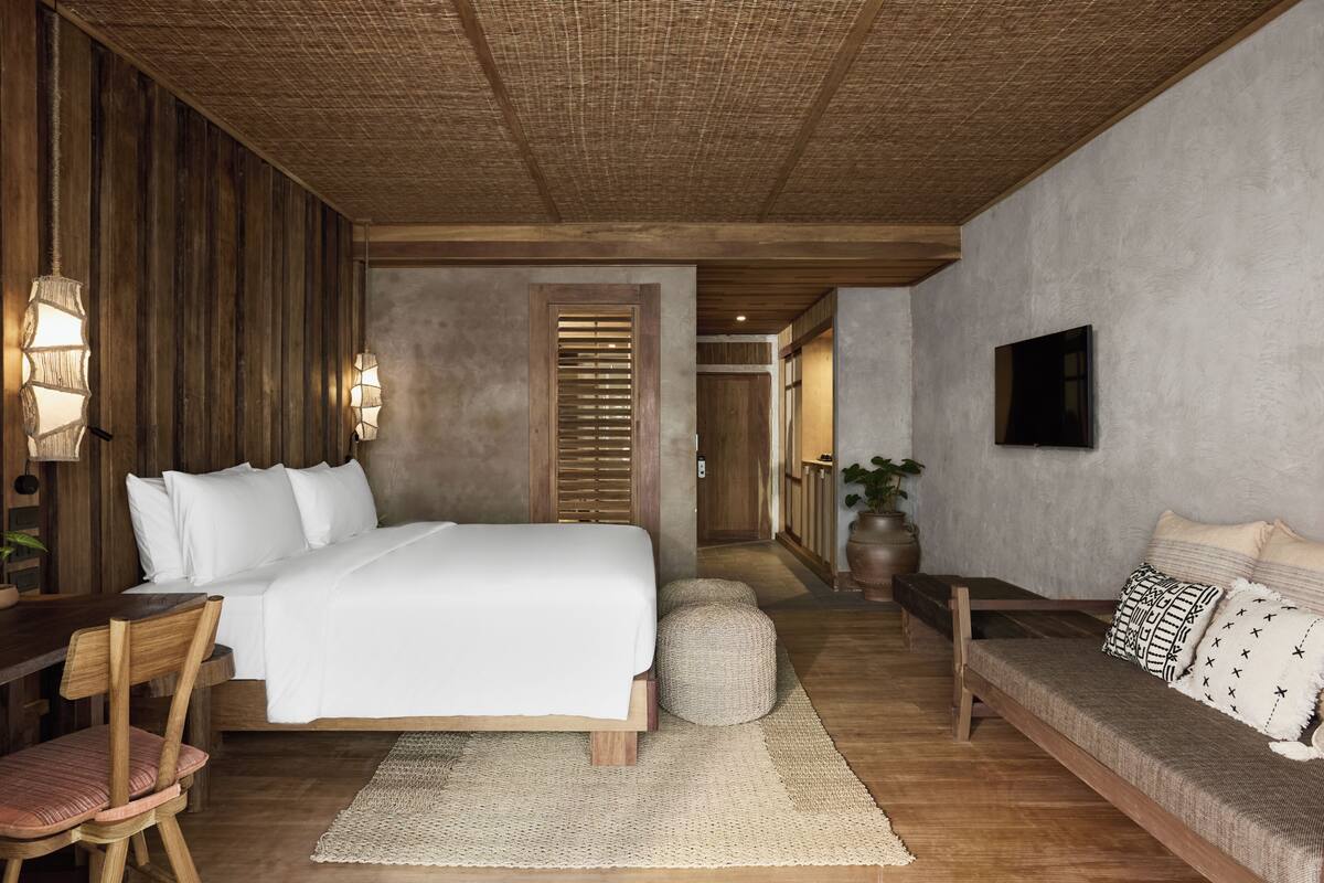 A bedroom with a bed, bedside table, chair, and a sofa.