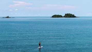A person paddleboarding on calm blue waters with small islands in the distance.