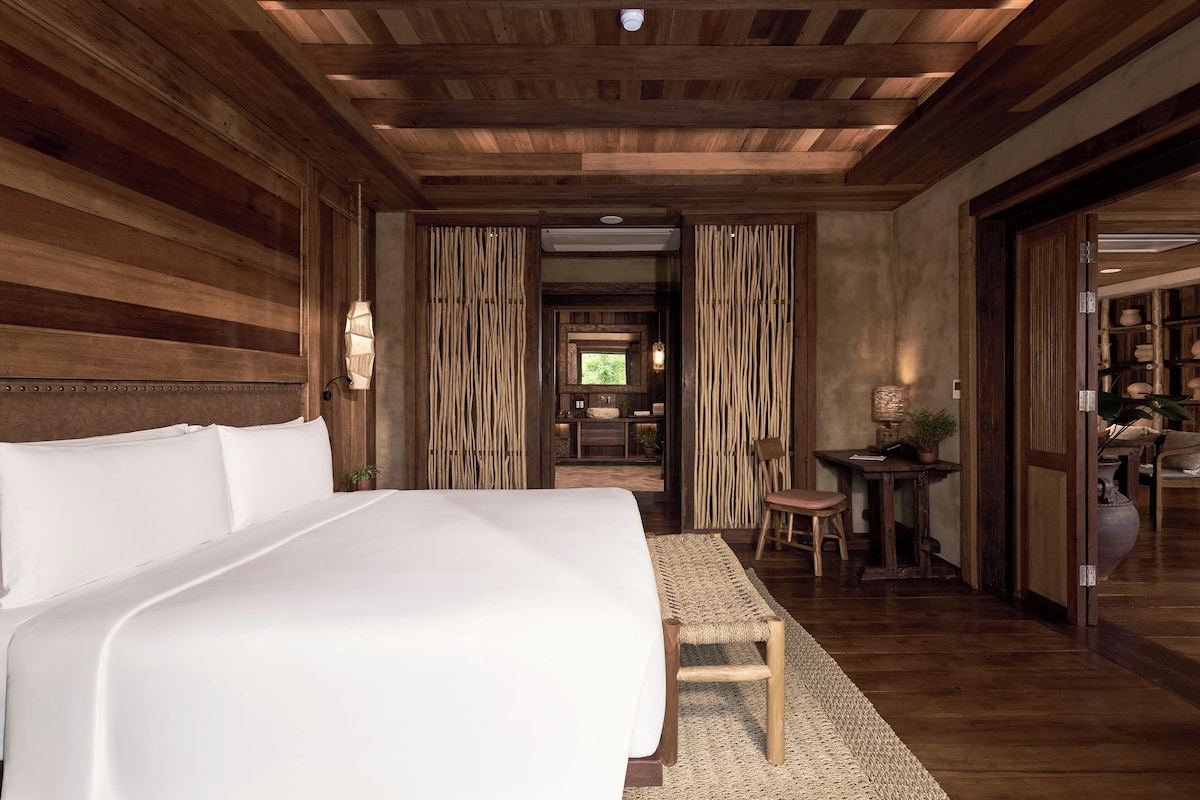 A bedroom with a large bed, wooden walls, and a ceiling with exposed beams.