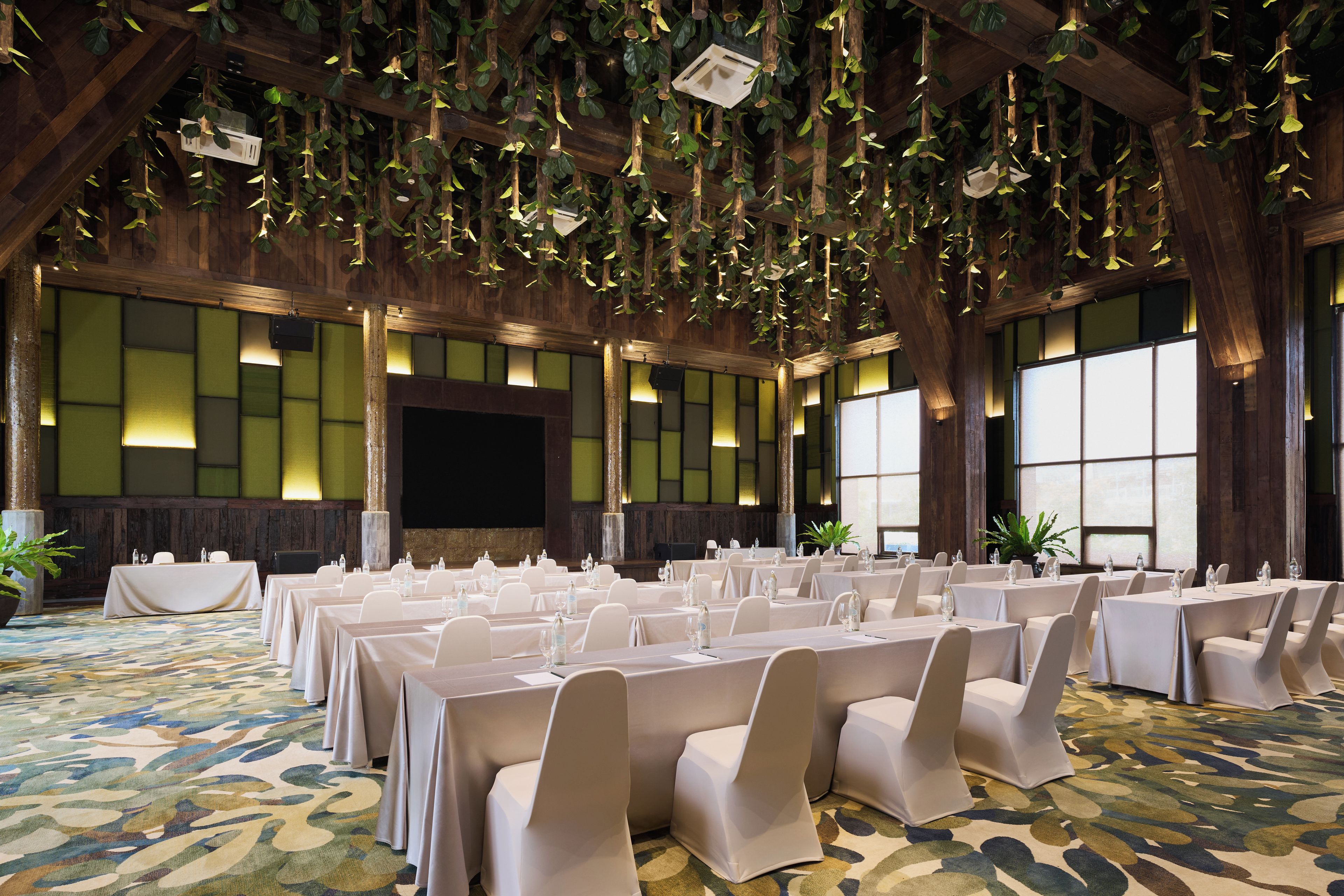 A banquet hall with tables set for events, a stage, and a large window.