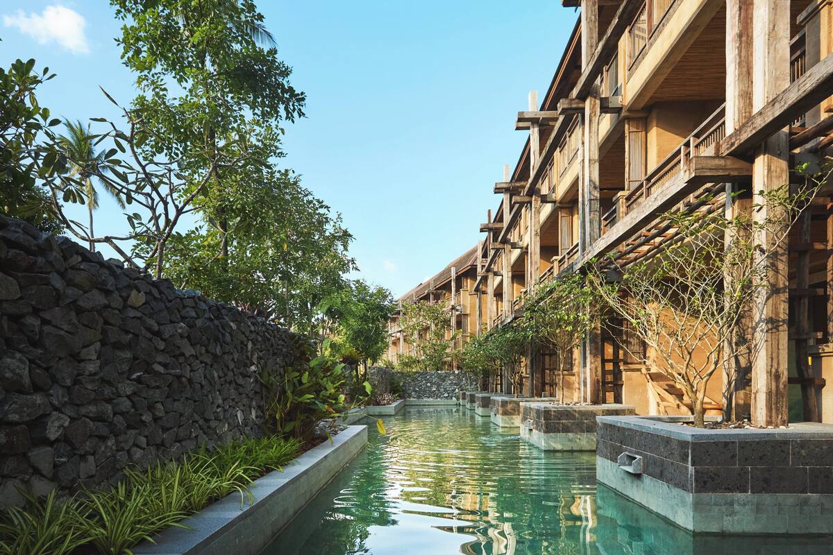 A courtyard with a pool, stone wall, and wooden buildings with balconies.