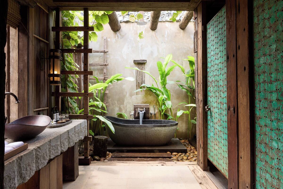 A rustic bathroom with a large stone sink, a freestanding bathtub, and a wooden vanity.
