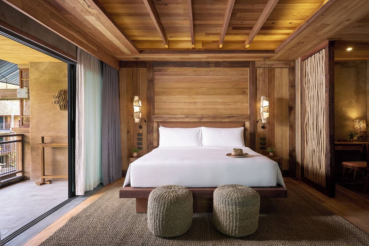 A wooden-paneled bedroom with a large bed, two wall-mounted lamps, and a view through a glass door.