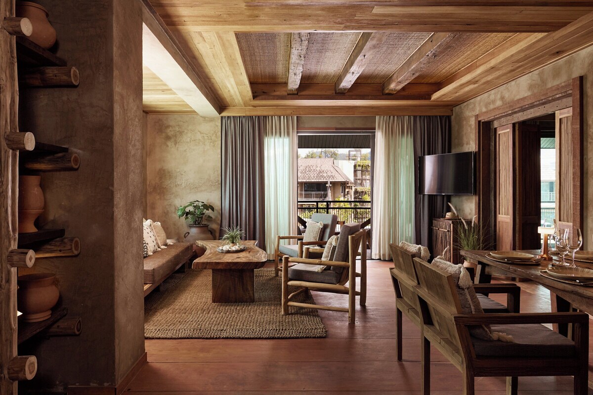A rustic room with a wooden ceiling, a sofa, chairs, a table, and a TV.