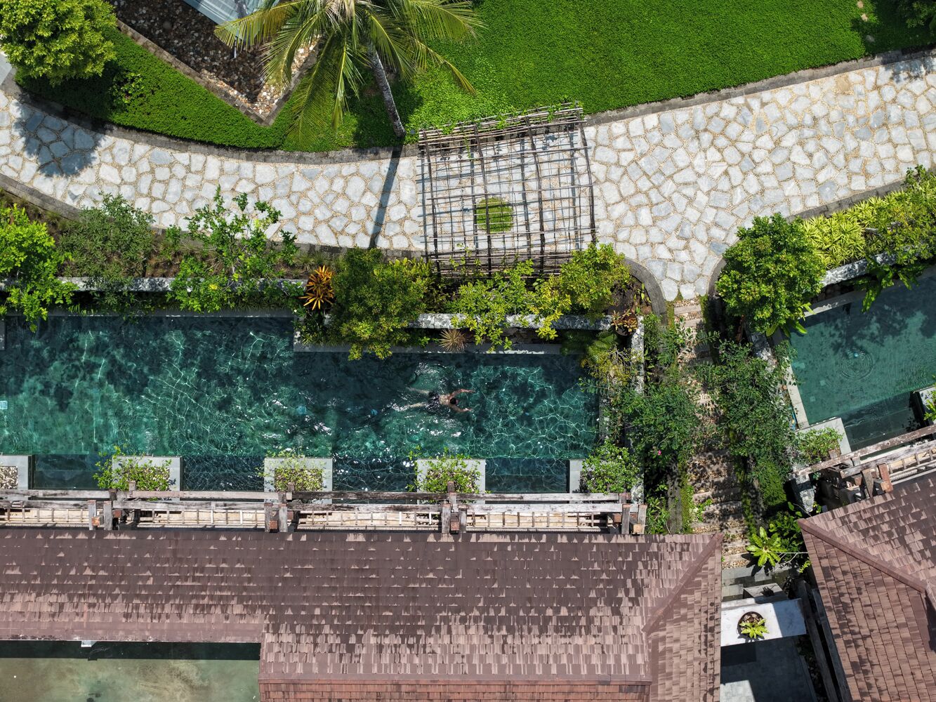 Vista aérea de una piscina con senderos de piedra y exuberante vegetación.