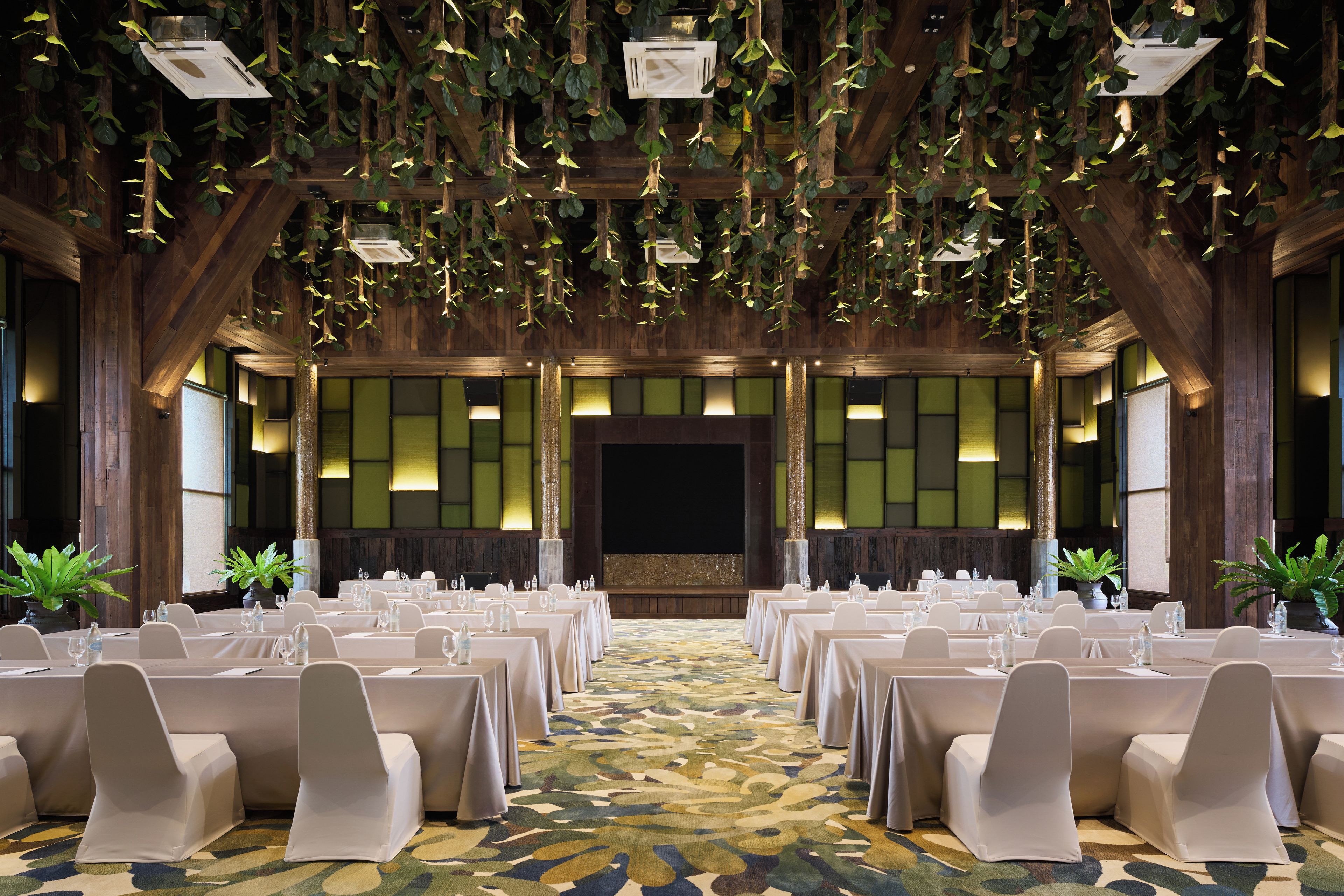 A banquet hall with long tables set for events, wooden beams, and hanging plants.