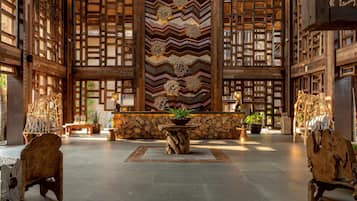 Een ruime lobby met een grote houten wand, een centrale stenen tafel met een plant en rustieke houten stoelen.