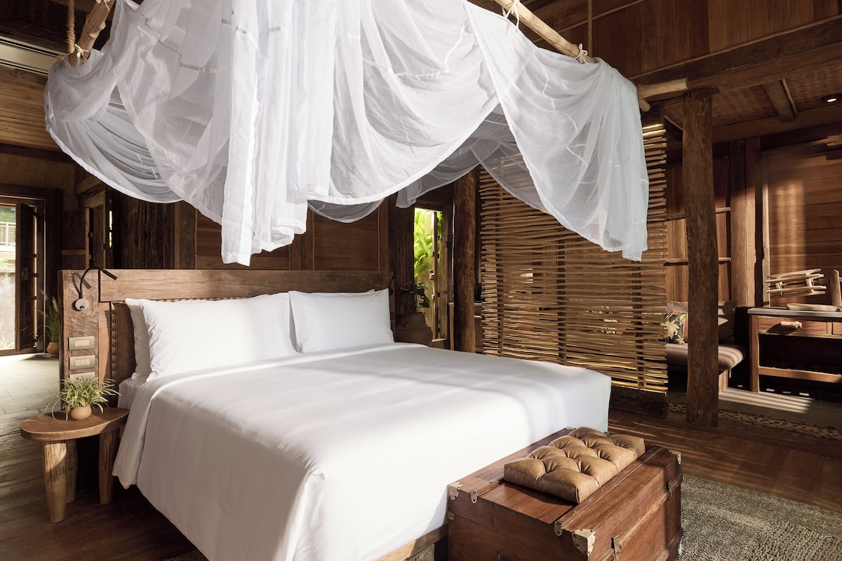 Una habitación de madera con una cama, un cofre de madera y un dosel colgante.