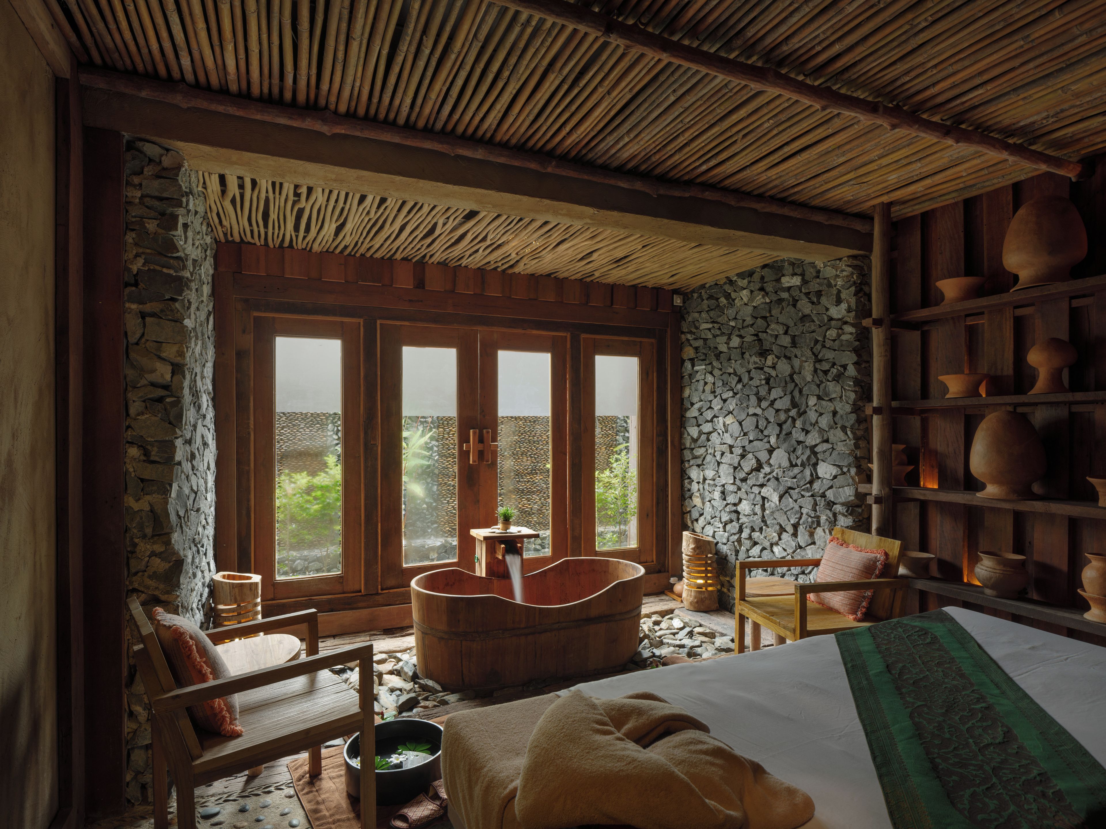 A room with a stone wall, wooden furniture, a large window, and a bamboo ceiling.