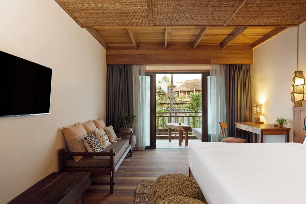 A hotel room with a bed, a sofa, a desk, a TV, and a balcony with a view of the outside.