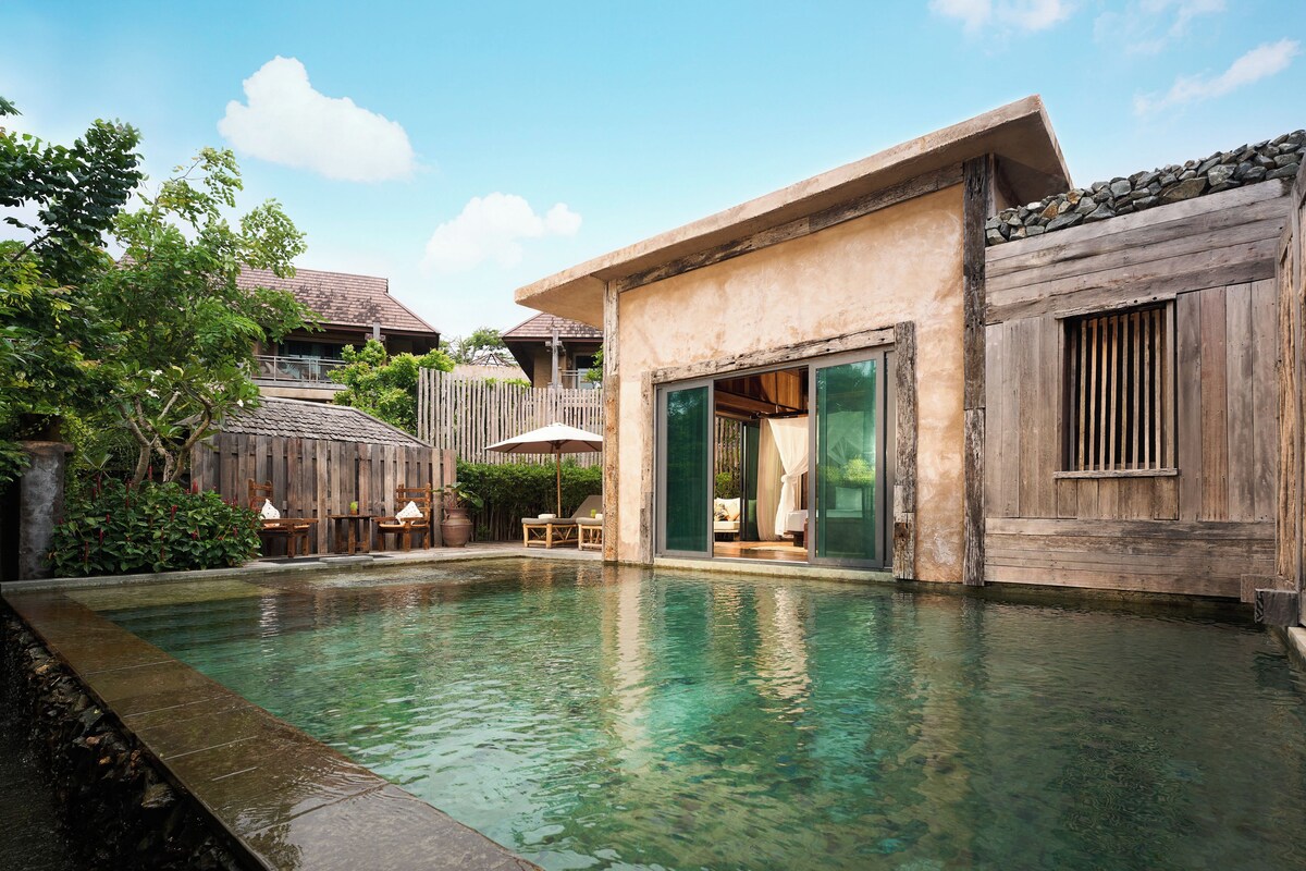 A pool area with clear water, wooden deck, and a view of a building with a balcony.