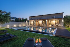 Une maison moderne dotée d’une piscine, de chaises longues et d’un patio bien aménagé et éclairé.