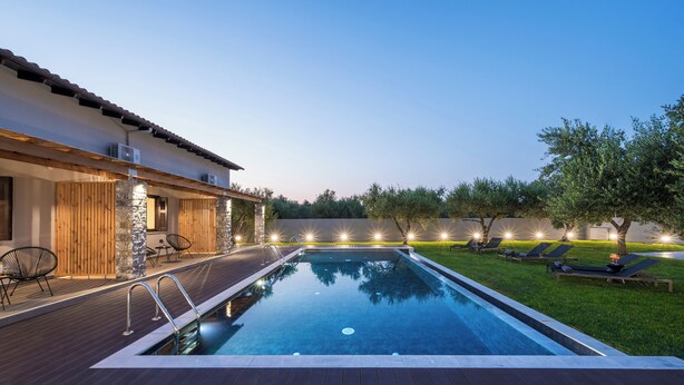 Una piscina con muelle de madera, sillas de descanso y un área de patio techada.