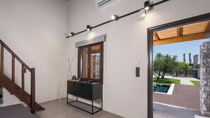 Un interior moderno con una escalera, una consola negra y vistas a un espacio exterior con piscina y vegetación.